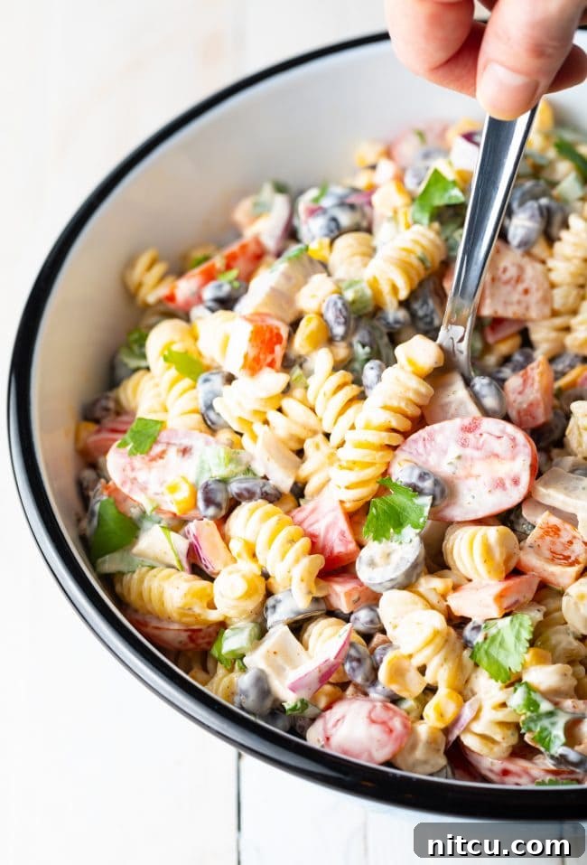 A hand holding a spoon and scooping creamy southwest pasta salad out of the salad bowl, showing its texture and ingredients.