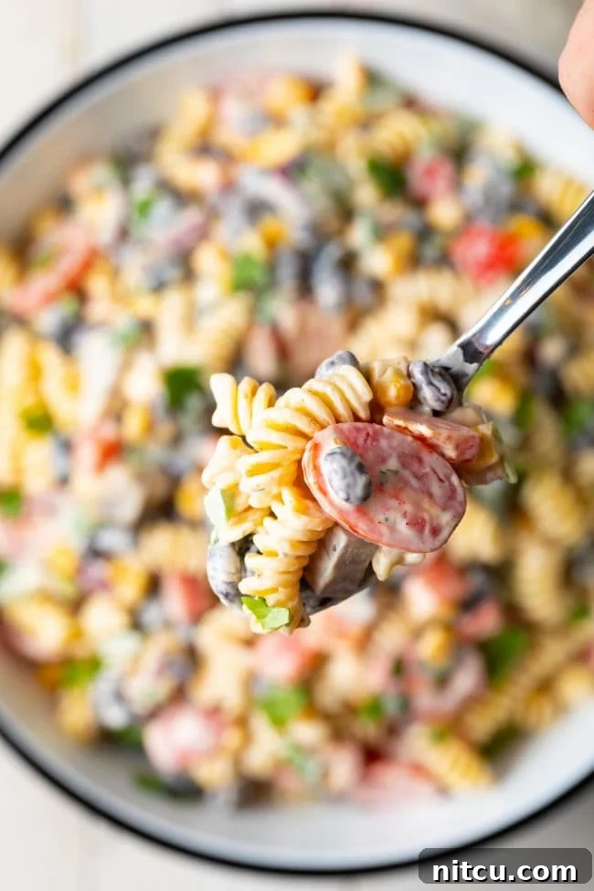 A hand holding a spoon with a scoop of creamy Southwest pasta salad over the serving bowl.
