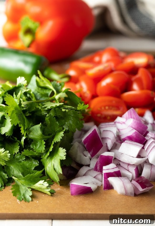 Chopped cilantro, red onion, grape tomatoes, and red bell pepper on a cutting board, ready for the salad.