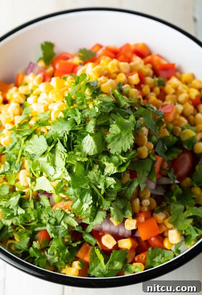 Bowl with fresh ingredients for pasta salad, including black beans, corn, and pasta.