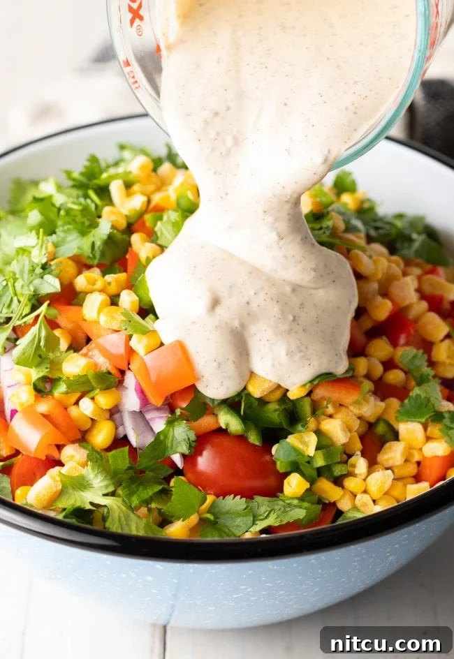 Creamy ranch dressing being poured over the salad ingredients in a large bowl.