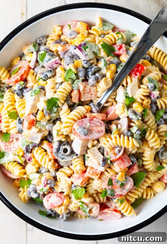 Pasta salad with creamy ranch dressing, colorful veggies, fresh cilantro, and black beans in a white serving bowl with a serving spoon.