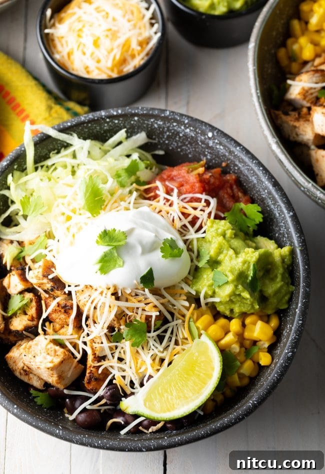 Close-up view of a homemade chicken chipotle burrito bowl, showing grilled chicken, rice, black beans, corn, and fresh toppings.