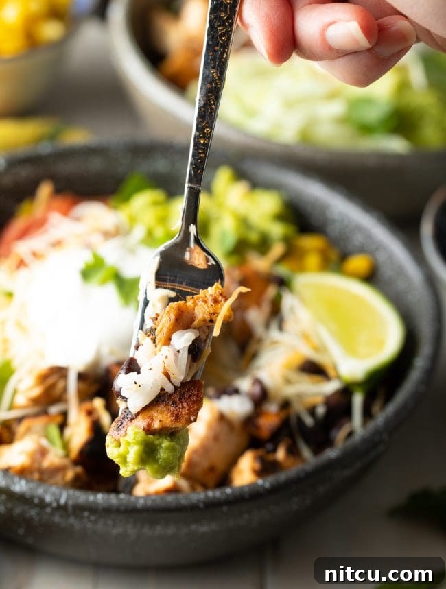 A spoonful of a homemade chipotle burrito bowl, showing a perfect bite of chicken, rice, and black beans.