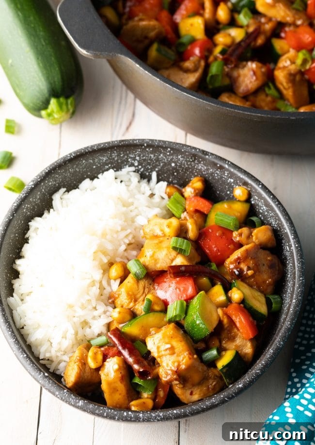 Authentic kung pao chicken with steamed white rice in a black bowl.