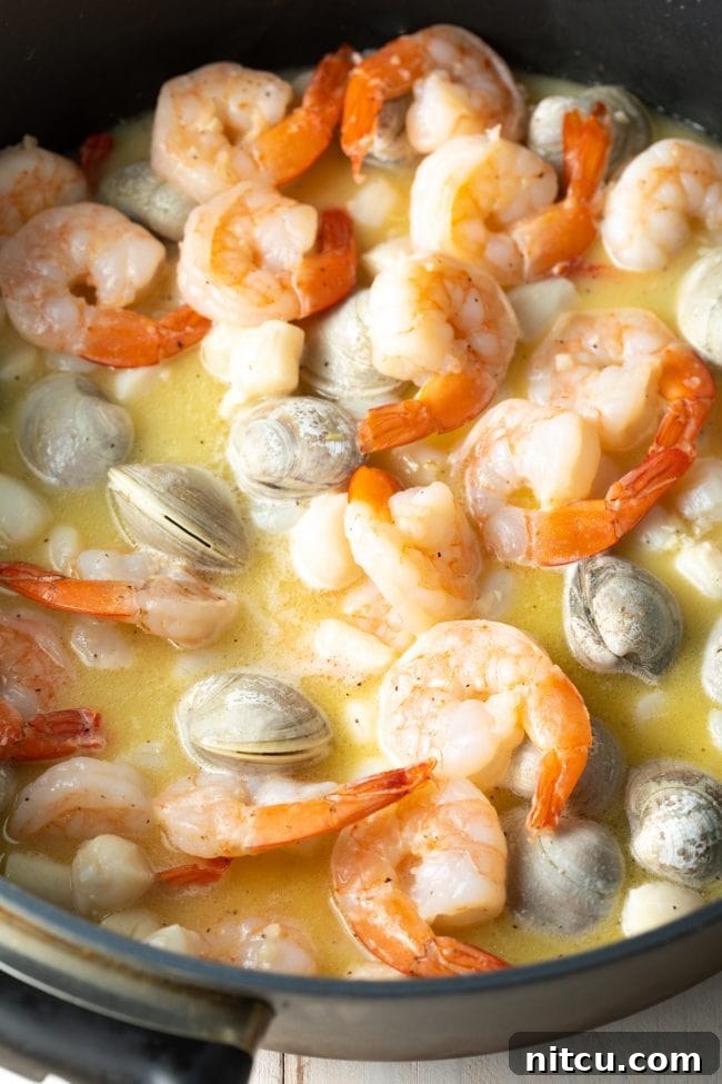 Fresh shrimp, scallops, and clams being sautéed in a skillet with melted butter and minced garlic.