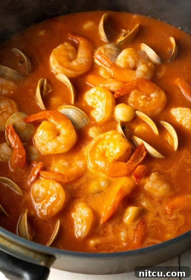 Shrimp, scallops, and clams simmering in a rich tomato and white wine sauce in a large skillet.