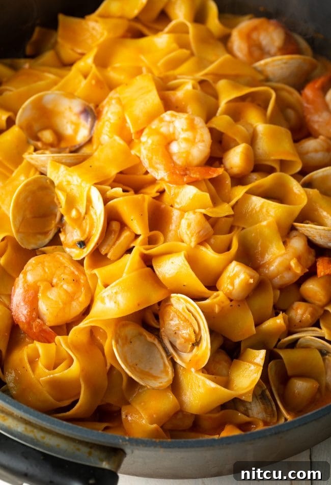 A close-up shot of broad pappardelle noodles beautifully tossed with a vibrant seafood and tomato sauce, showcasing the rich texture and fresh ingredients.