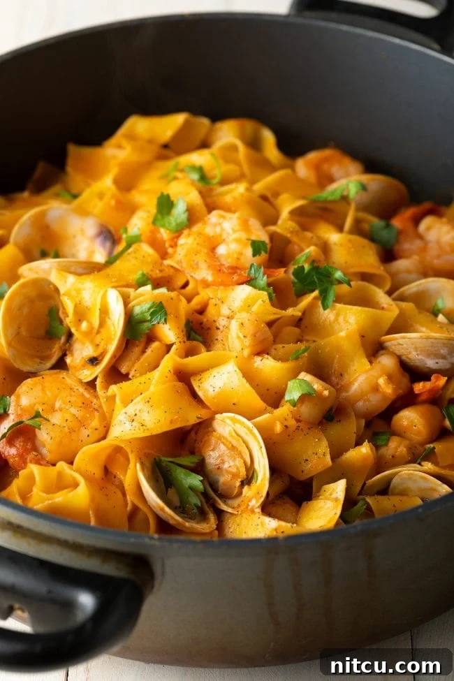 Large cooking pot filled with wide egg noodles coated in a rich, creamy seafood and tomato sauce, ready to be served.