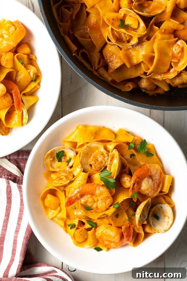 Top-down view of a generously sized serving of seafood pappardelle in a pristine white bowl, garnished with fresh herbs.