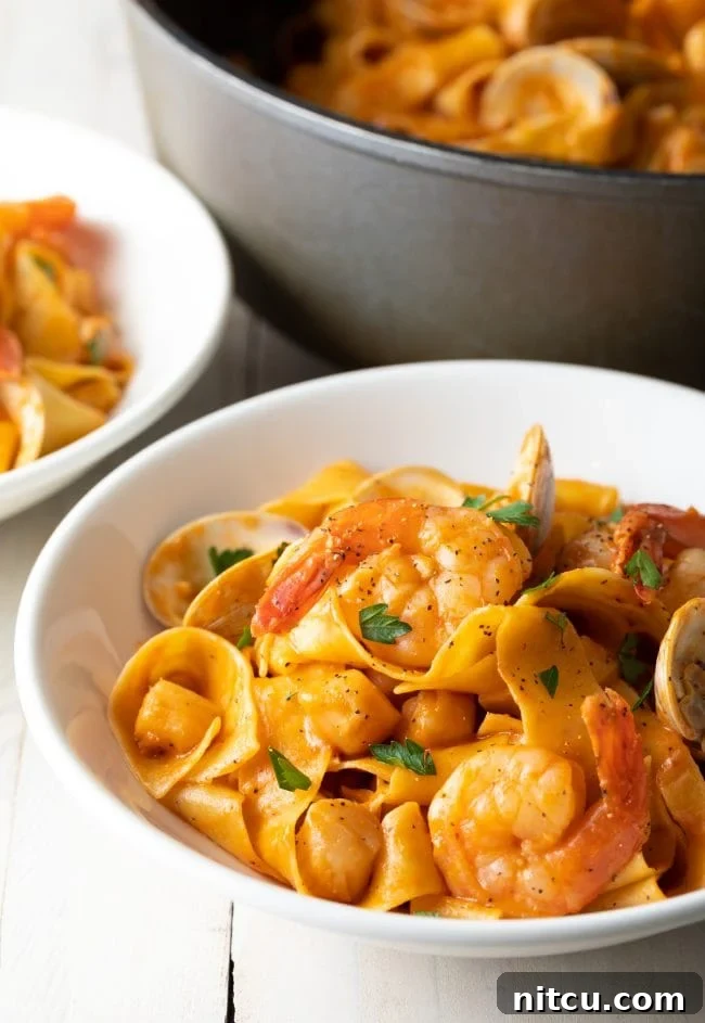 A vibrant close-up of a serving of seafood pappardelle in a white bowl, showcasing the rich sauce and perfectly cooked seafood.