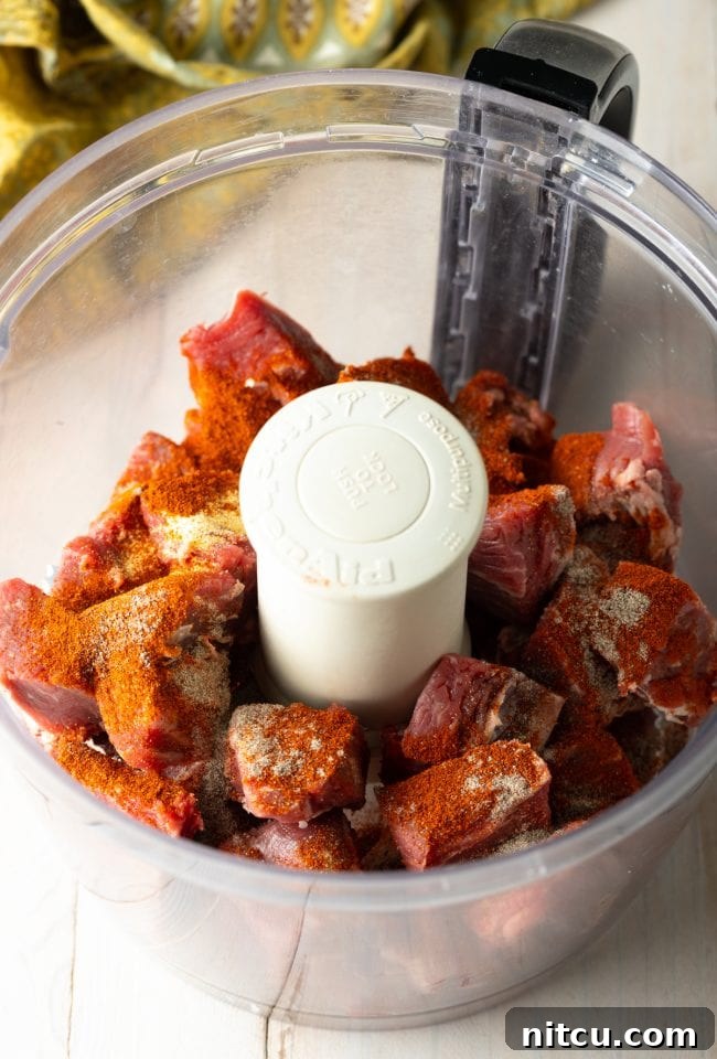 Chunks of high-quality steak being processed with seasonings in a food processor.
