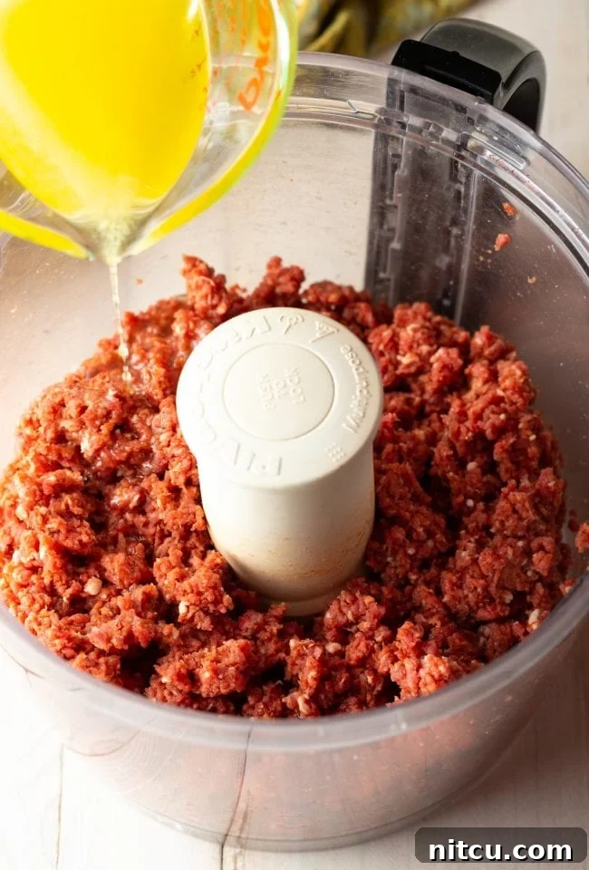 Adding clarified butter to chopped steak tartare in a food processor bowl.