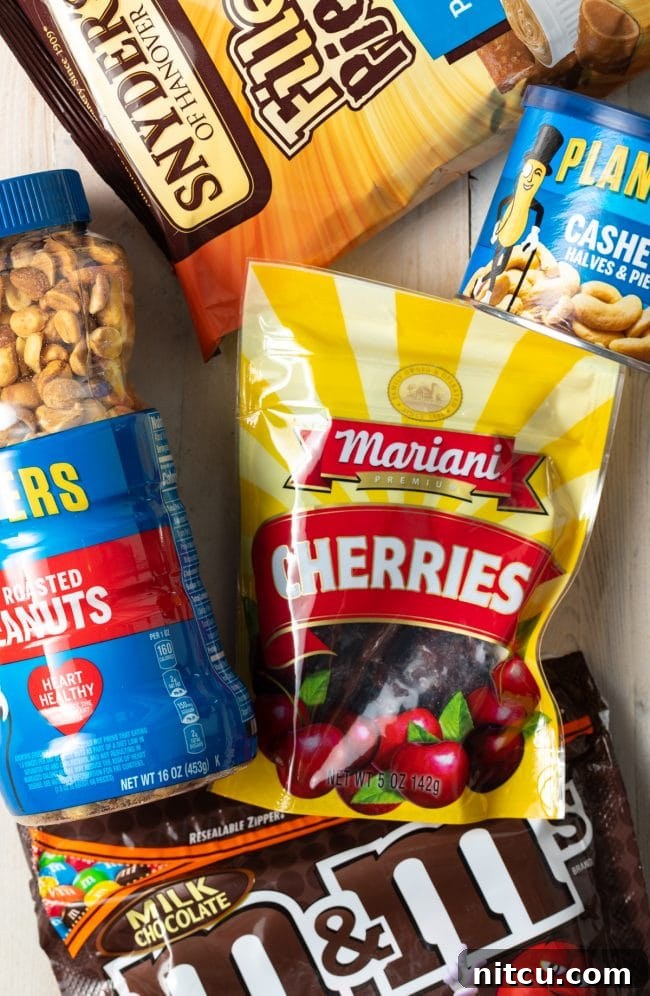 Close-up of indulgent trail mix ingredients: dried cherries, cashews, peanuts, peanut butter pretzels, and colorful M&M candies.
