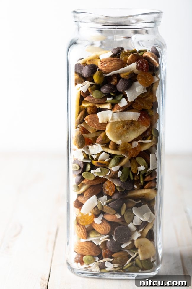 A side view of a stylish glass jar filled with healthy trail mix, showcasing its layers.