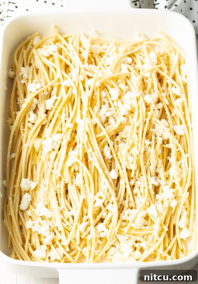 Soaked bucatini in a white baking dish, topped with crumbled Greek feta cheese.