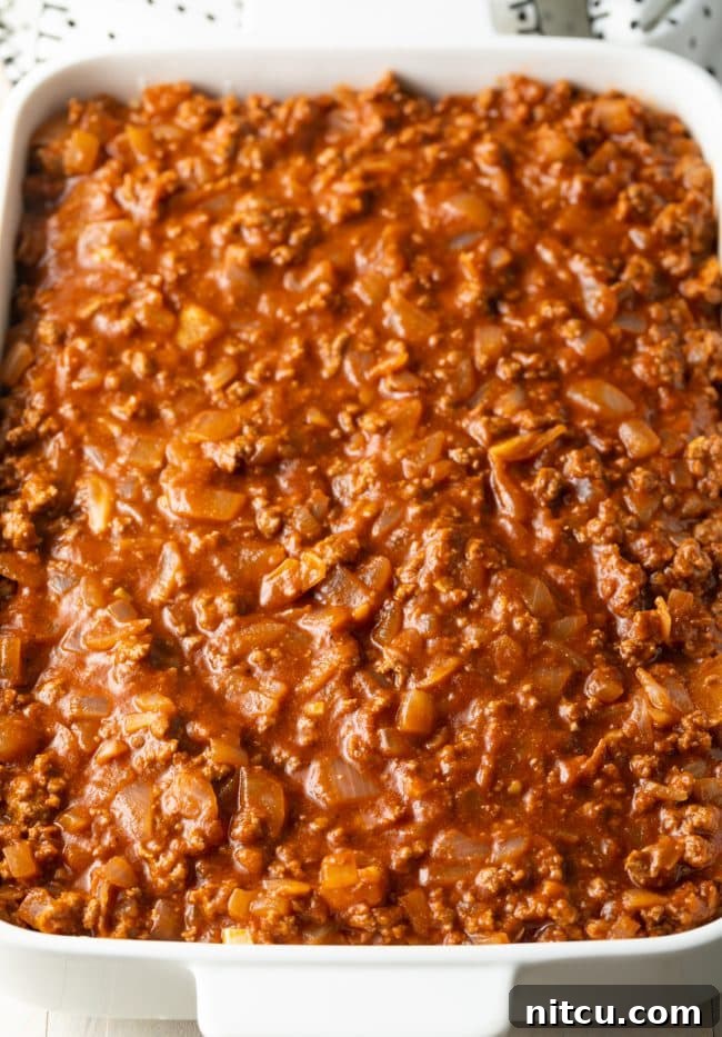 Zesty tomato meat sauce poured on top of pasta in a white baking dish.