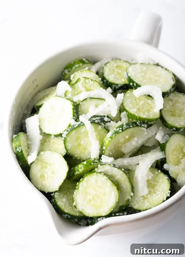 White bowl with sliced cucumbers and white onion.