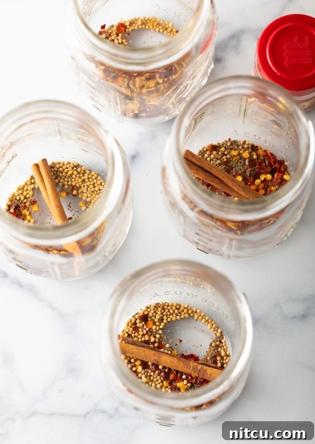 Four glass jars with cinnamon sticks and mustard seeds.
