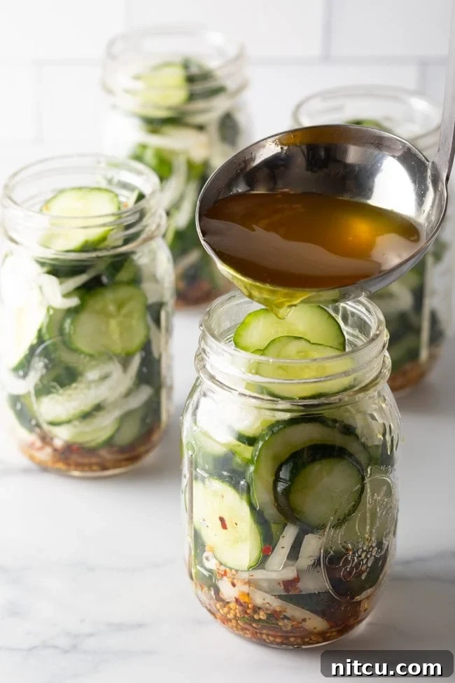 Using a metal ladle to pour pickling liquid into glass jars with sliced cucumbers and onions.