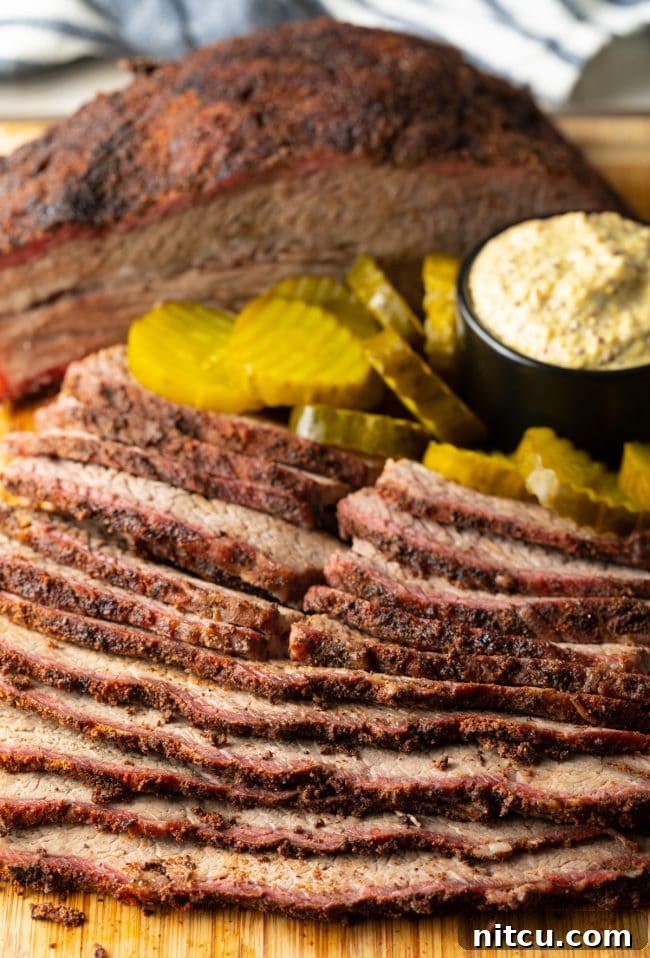 Smoked beef brisket perfectly sliced on a wooden cutting board, accompanied by pickles and mustard for serving.