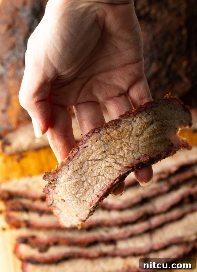 Close-up of a hand holding a perfectly sliced piece of smoked brisket, showing its juicy interior and smoke ring.