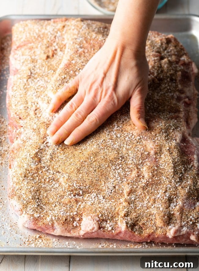 A hand rubbing the dry brisket brine spices onto the meat, ensuring even coverage.