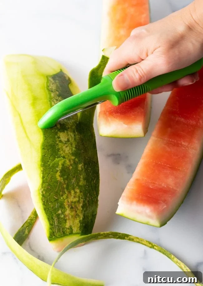 Hand peeling the green layer off of a watermelon rind.