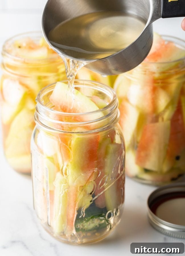pouring the pickling brine into the jars filled with watermelon rinds, jalapeños and peppercorns.