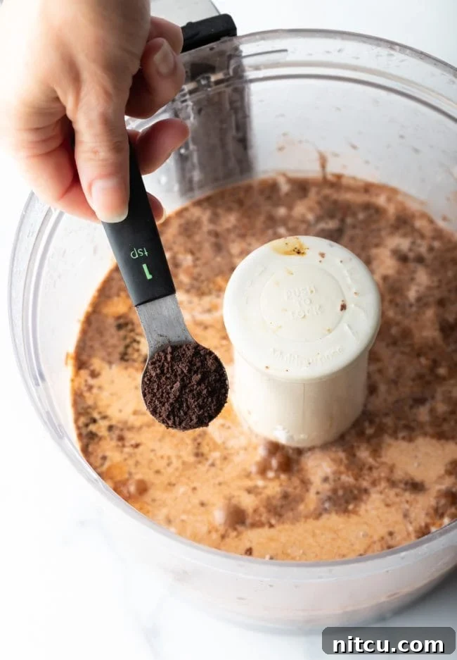Spreading the cream cheese layer over the Oreo crust in a baking dish.