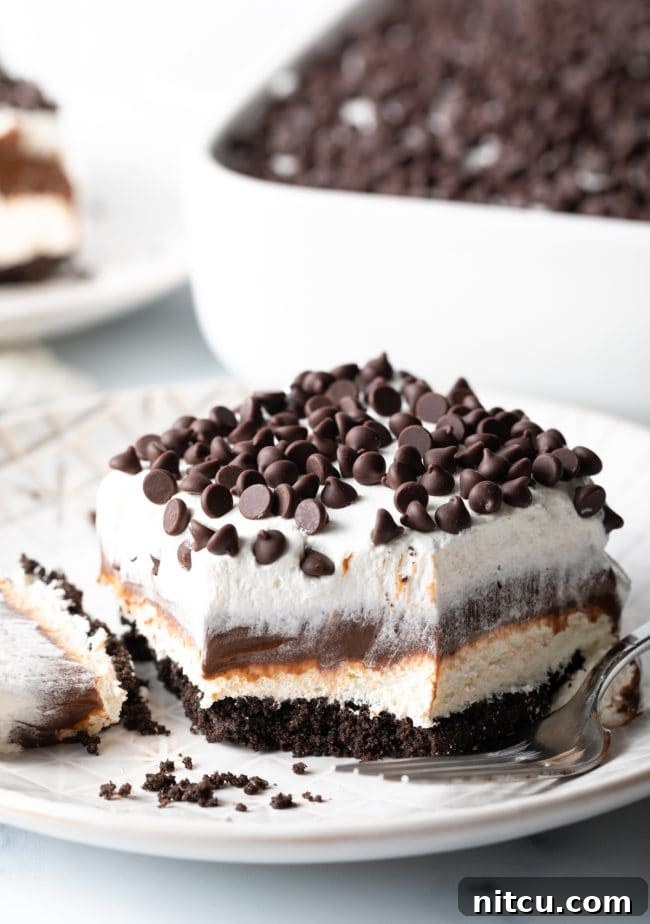 A slice of No-Bake Chocolate Lasagna with a bite taken out, showing the perfect layering of Oreo crust, cream cheese, chocolate pudding, and whipped topping.