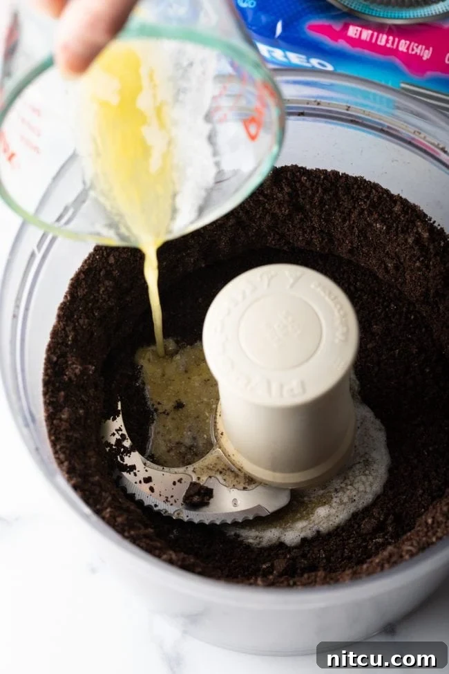 Melted butter being added to crushed Oreos in a food processor.