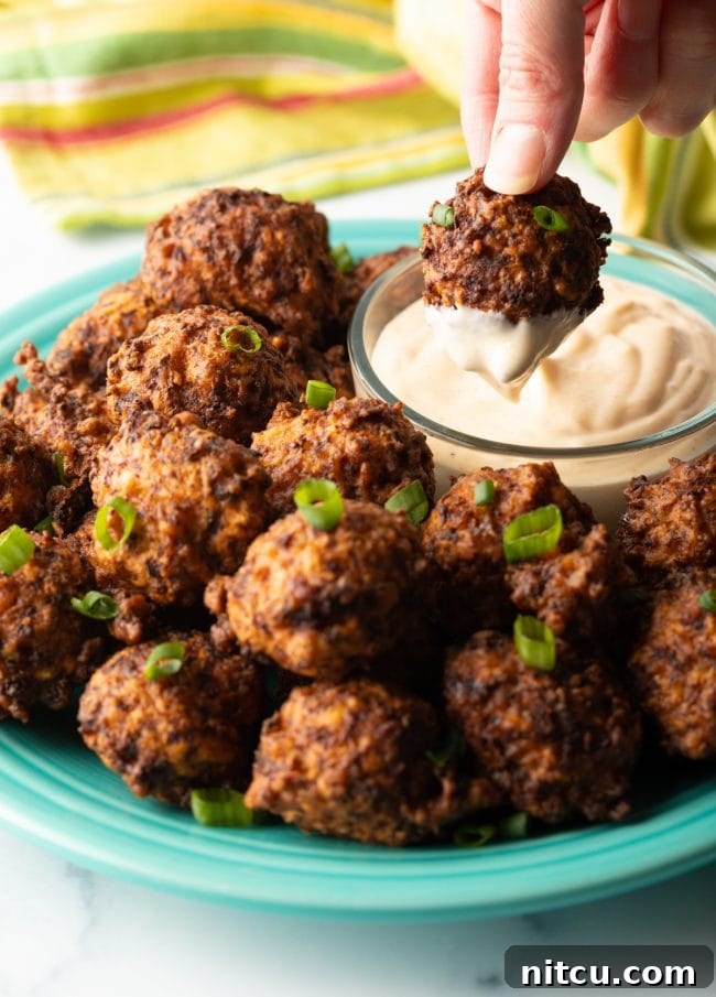 A hand dipping a crispy Bahamian conch fritter into a creamy remoulade sauce, showcasing the perfect texture and inviting appeal of the appetizer.