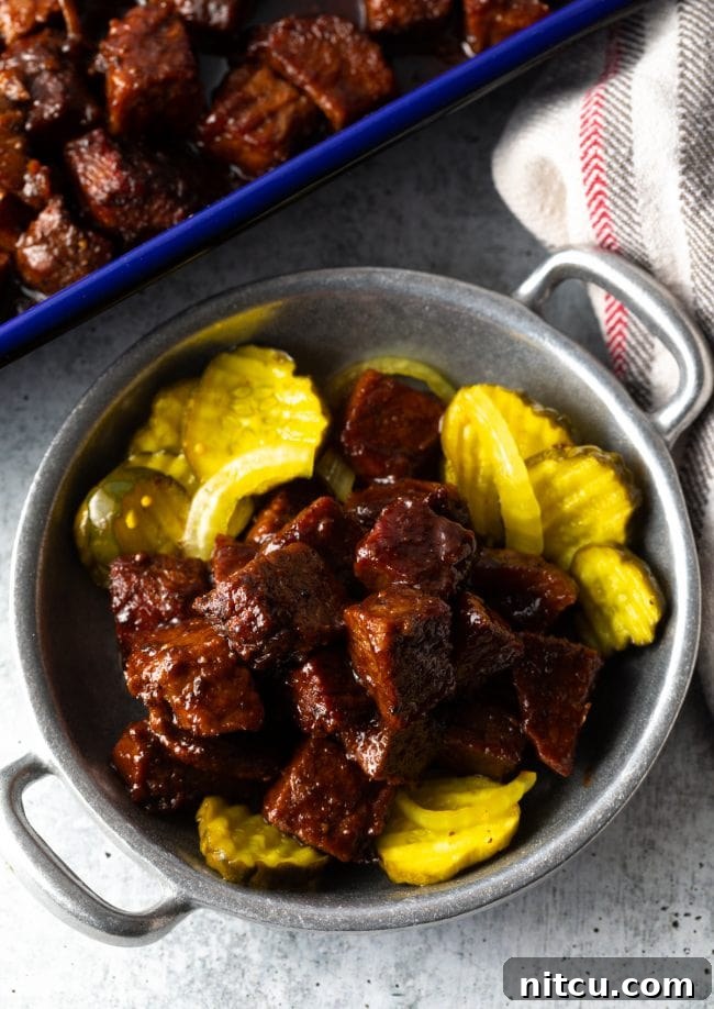 Irresistible Brisket Burnt Ends in BBQ sauce, garnished with fresh pickles, ready to be served.