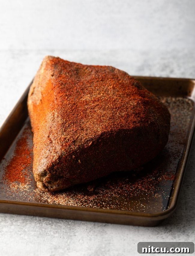 Seasoned hunk of beef brisket on a baking sheet, ready for slow cooking in the smoker or oven.