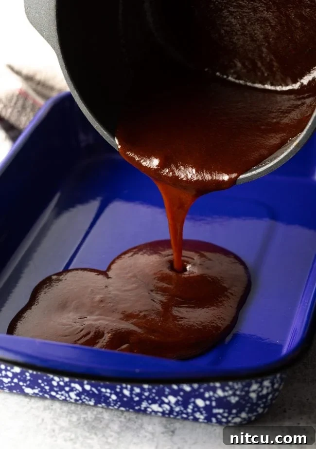 Pouring rich barbecue sauce into a large blue baking pan, preparing for the burnt ends braise.