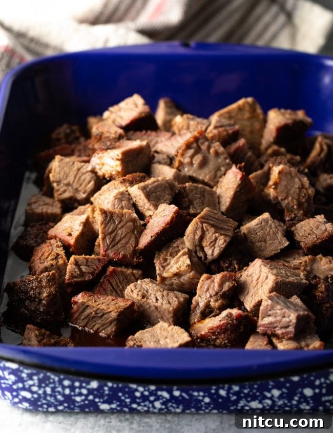 Tender chunks of smoked brisket bathing in barbecue sauce within a blue pan, ready for their final cook.