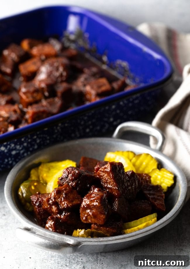 A metal bowl overflowing with savory brisket burnt ends, accompanied by slices of fresh bread and crisp butter pickles.