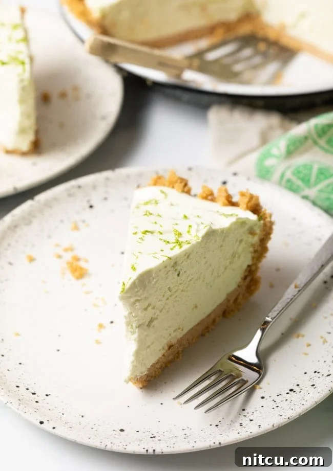 A vibrant slice of no-bake key lime pie presented on a pristine white plate, accompanied by a fork, ready to be enjoyed.