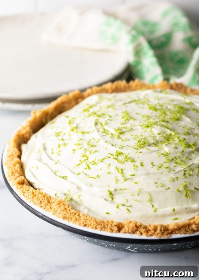 A beautifully garnished key lime icebox pie, complete with a fresh dusting of lime zest, presented in its pie pan, ready to be sliced and served as a refreshing dessert.