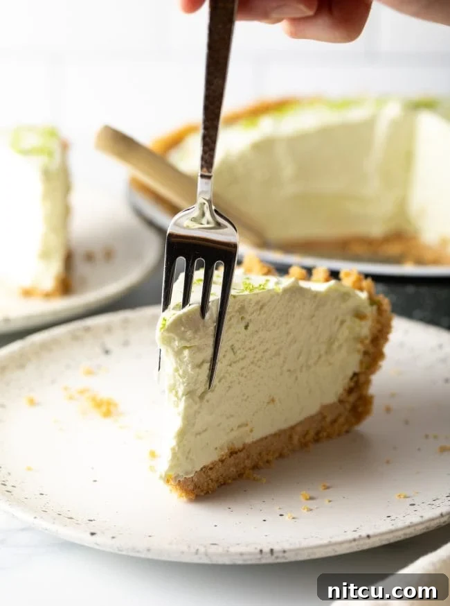 A delicious slice of key lime pie on a plate with a fork, showing a bite already taken, highlighting the creamy texture and inviting taste.