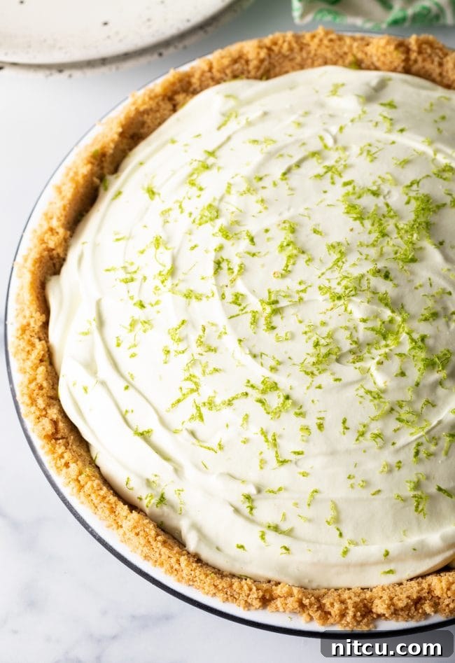 A perfectly prepared full no-bake key lime icebox pie, featuring a golden graham cracker crust and generously sprinkled with fresh lime zest on top, waiting to be sliced.