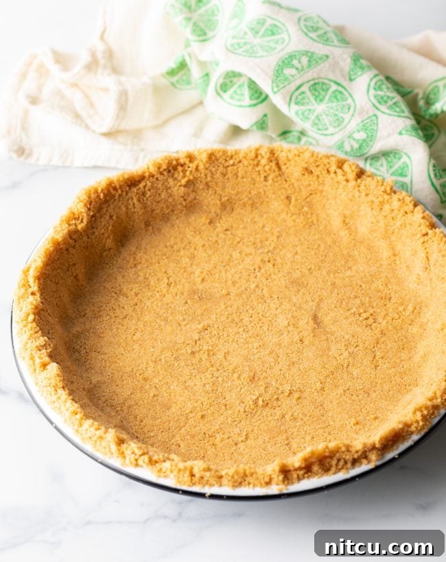 A neatly pressed graham cracker crust mixture forming an even layer in a pie plate, prepared and chilled, awaiting its delicious filling.