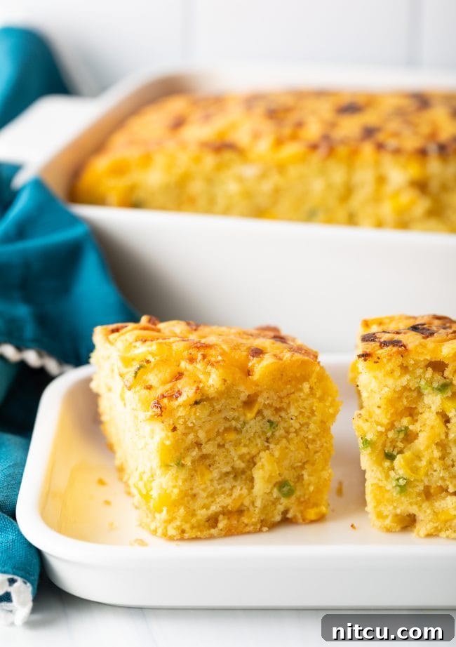 Side view of jalapeno cornbread squares filled with chopped peppers and topped with melted cheese, showcasing its rich texture.