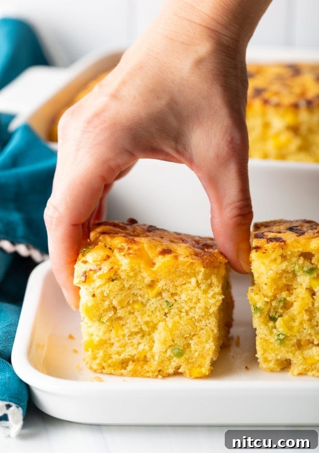 A hand reaching for a piece of this delectable jalapeno cheddar cornbread, highlighting its golden crust and inviting texture.