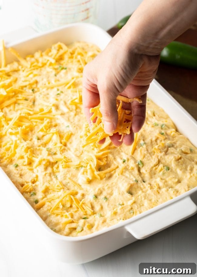 Cornbread batter scooped into a baking dish, ready for the final cheese sprinkle.
