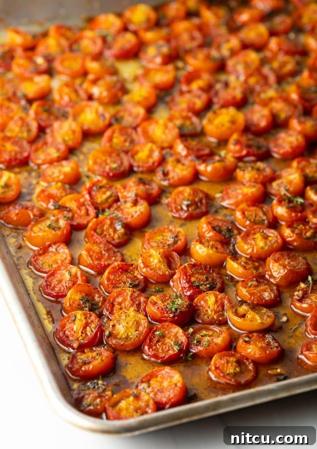 Roasted cherry tomatoes on a baking sheet, glistening with balsamic glaze.