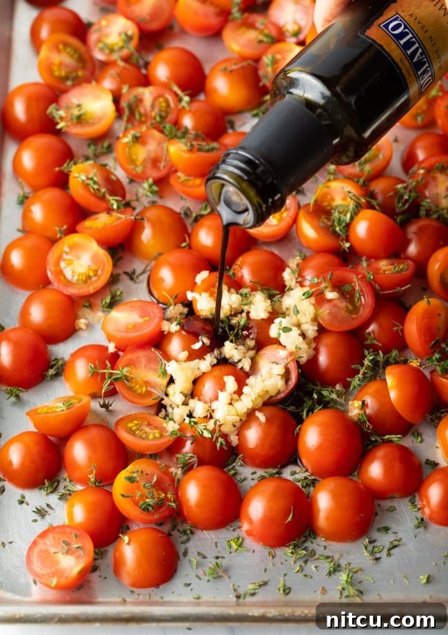 Pouring rich balsamic vinegar over a bed of cherry tomatoes on a baking pan.