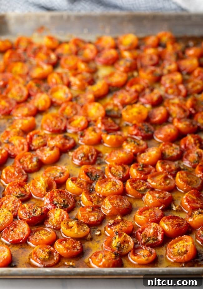 Close-up side view of perfectly oven-roasted cherry tomatoes on a baking sheet, with visible juices.