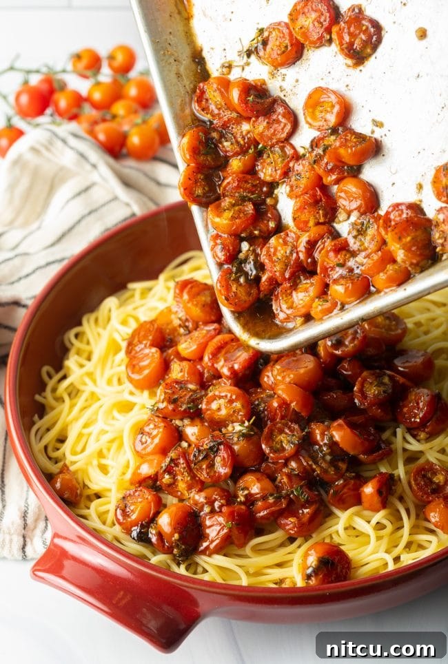 A cook pouring the succulent roasted tomatoes from the baking sheet directly onto a bed of cooked spaghetti.